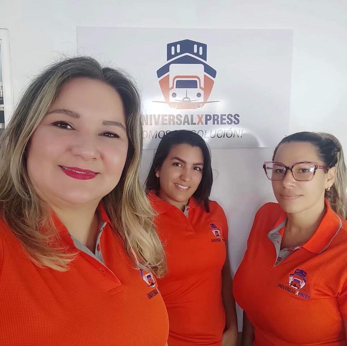 Equipo de Universal Xpress con el uniforme de la marca frente al logo de la agencia